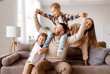 Junge Familie mit zwei Kindern. Junge sitzt auf den Schultern des Vaters. Mutter und Tochter sehen lachend in die Kamera.