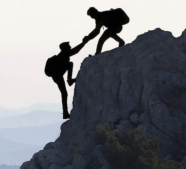 Zwei Personen erklimmen Berg und helfen sich dabei gegenseitig