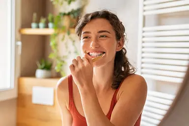 Frau lächelt beim Zähne putzen mit Zahnzusatzversicherung vom Testsieger