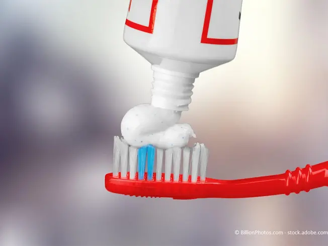 Weiße Zahnpasta, aufgetragen auf einer roten Zahnbürste vor verschwommenem Hintergrund.