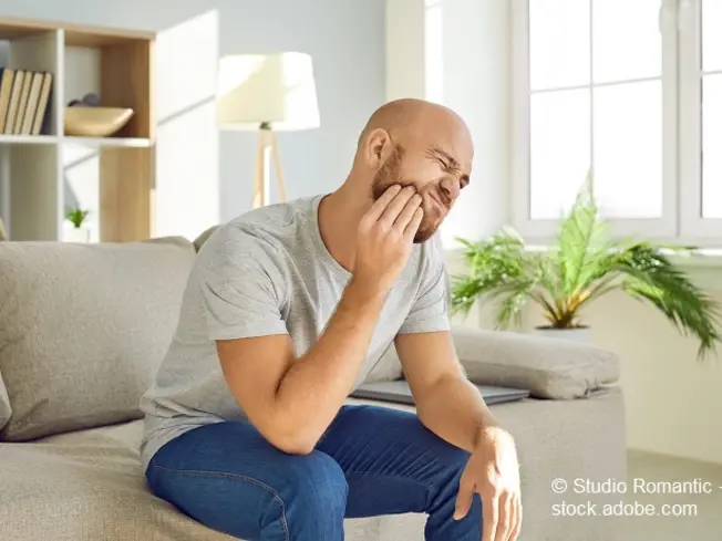 Mann sitzt mit Zahnschmerzen auf der Couch.