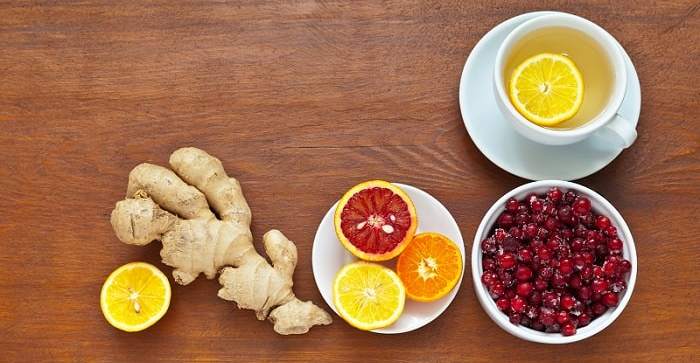 Tee, Ingwer, Zitrone, Orange und Cranberry platziert auf einem Holztisch.