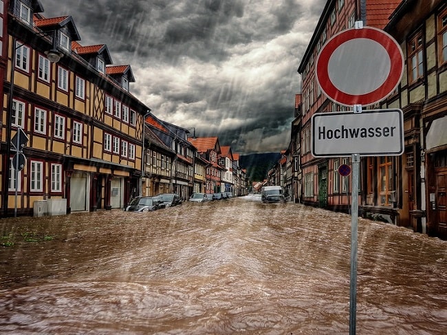 Bild einer überfluteten Straße auf der ein Schild mit dem Wort "Hochwasser" steht.